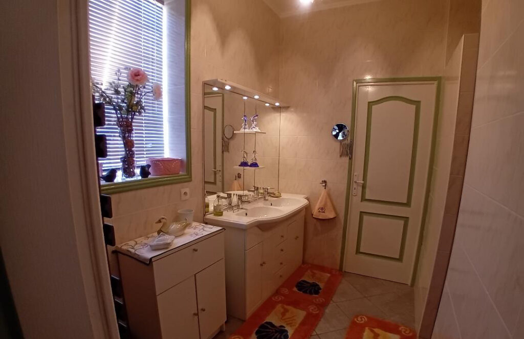 Salle de bain propre et lumineuse avec vasque, grand miroir et rangements dans un logement de La Roseraie